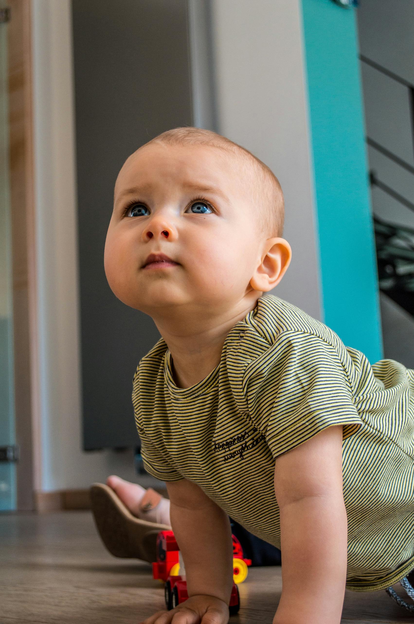 Adorable baby with blue eyes looking up while crawling indoors, showcasing innocence and curiosity.