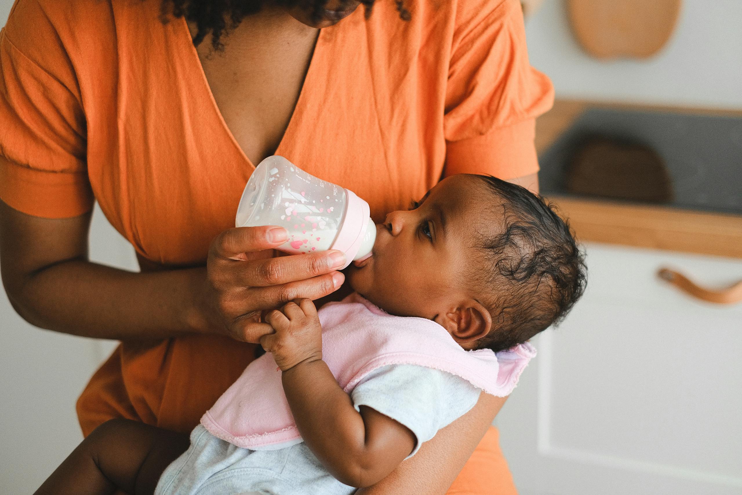 Close-up of a mother feeding her baby with a bottle in a warm home setting.